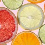 Komar Fototapete Vlies Fresh, 100x280 cm, mit bunten Zitrusfrucht-Scheiben auf rosa Hintergrund.