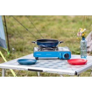 Campingaz Camp Bistro DLX Tischkocher mit Pfanne, Teller und Blumenvase auf einem Campingtisch.