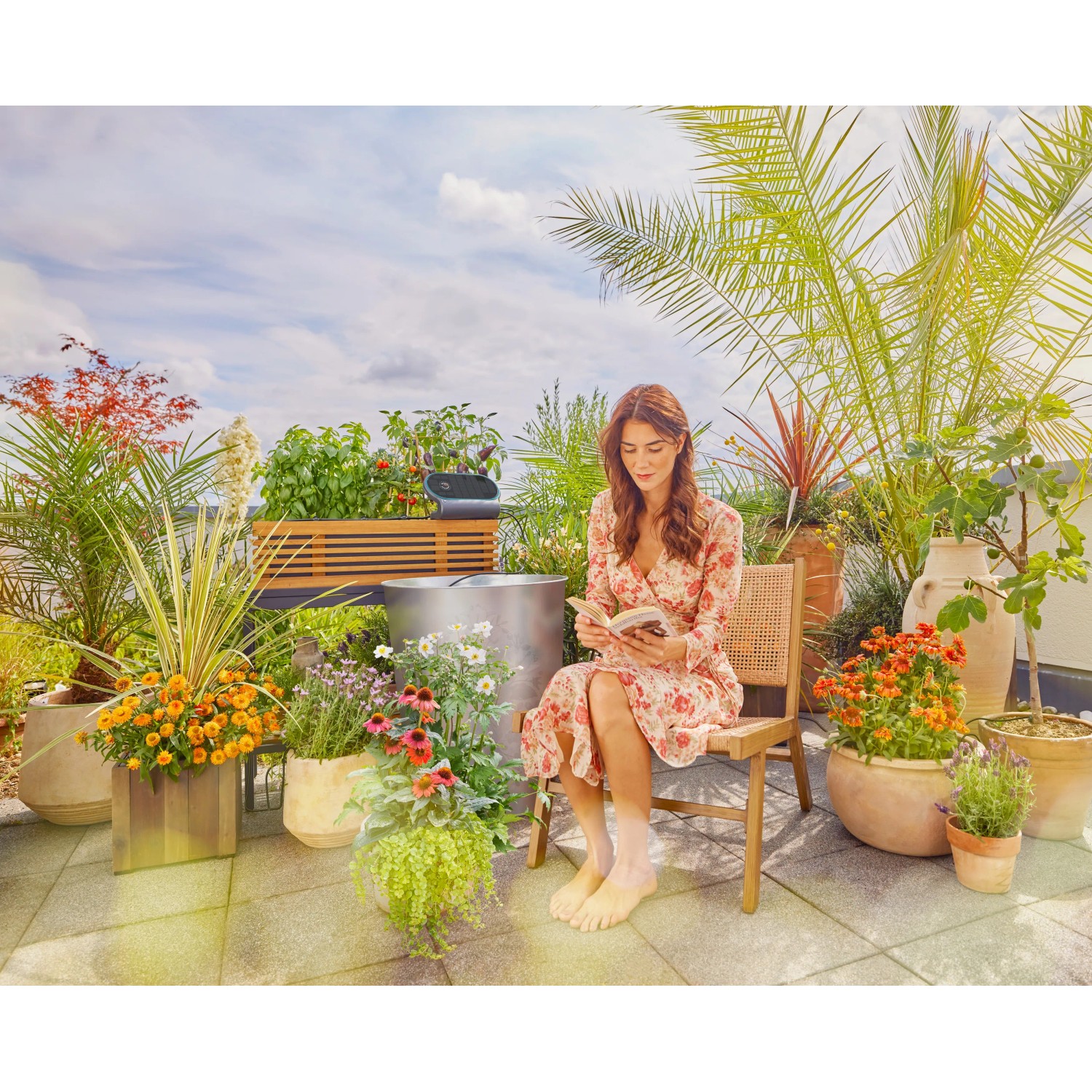 Frau liest auf Terrasse mit Gardena AquaBloom L Solar-Bewässerung für bis zu 30 Pflanzen.