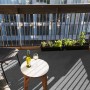 Grauer Primaflor Rasenteppich auf Balkon mit Tisch, Wein und Pflanzen.