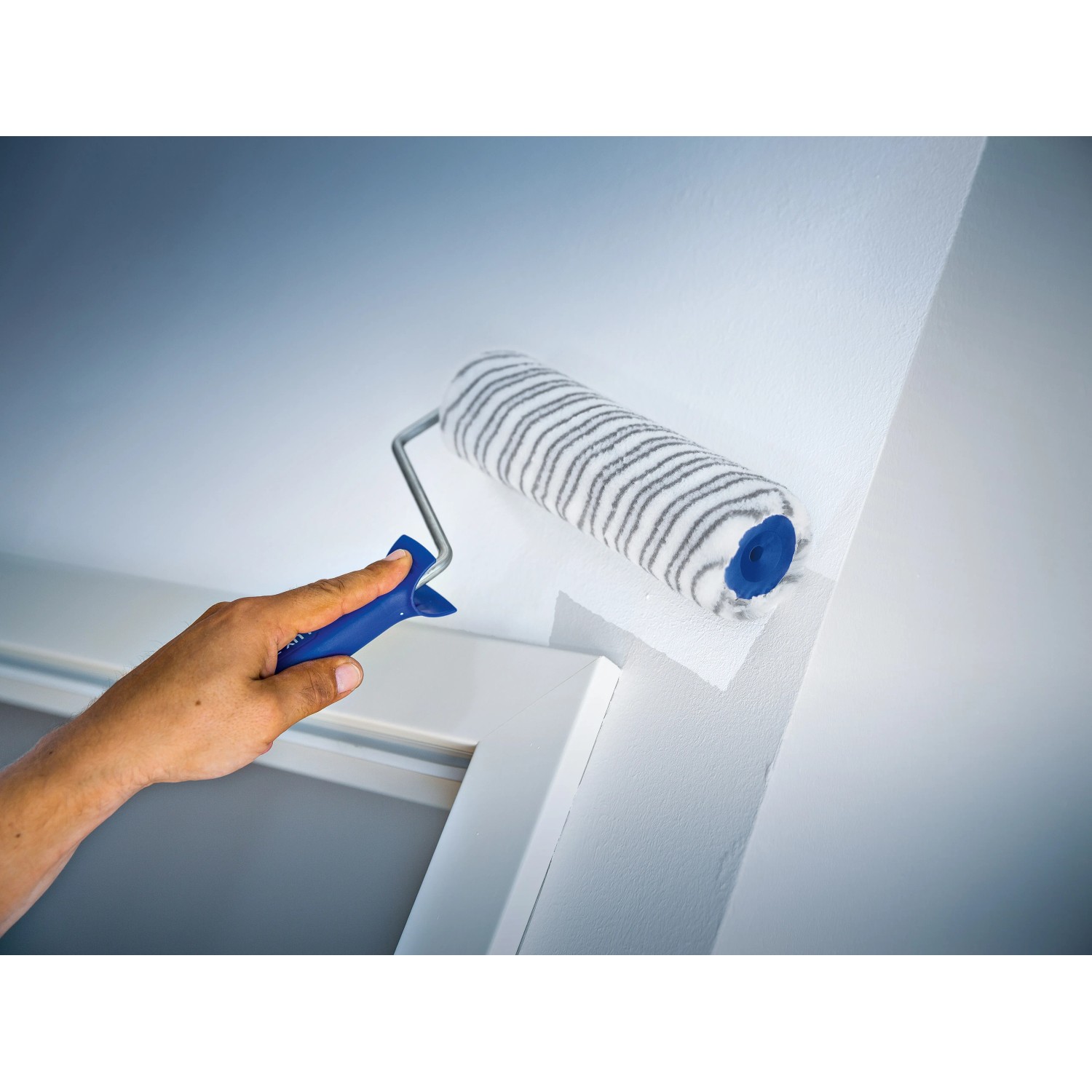 LUX Dispersionswalze 18 cm beim Streichen einer Wand, Farbwalze mit grau-gestreiftem Kurzflor.