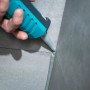 Hand dichtet Fliesenfuge mit wolfcraft Kartuschenspitze und grauem Dichtstoff ab.