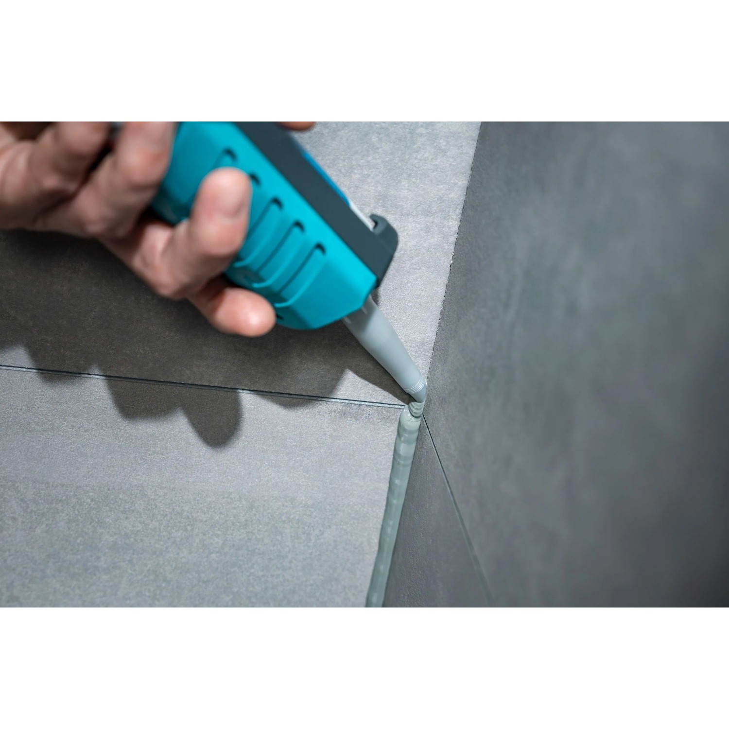 Hand dichtet Fliesenfuge mit wolfcraft Kartuschenspitze und grauem Dichtstoff ab.