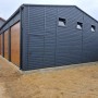 Liderstal Blechhalle 12x8m, graphit, mit drei Sektionaltoren in Goldene Eiche und kleinen Fenstern.