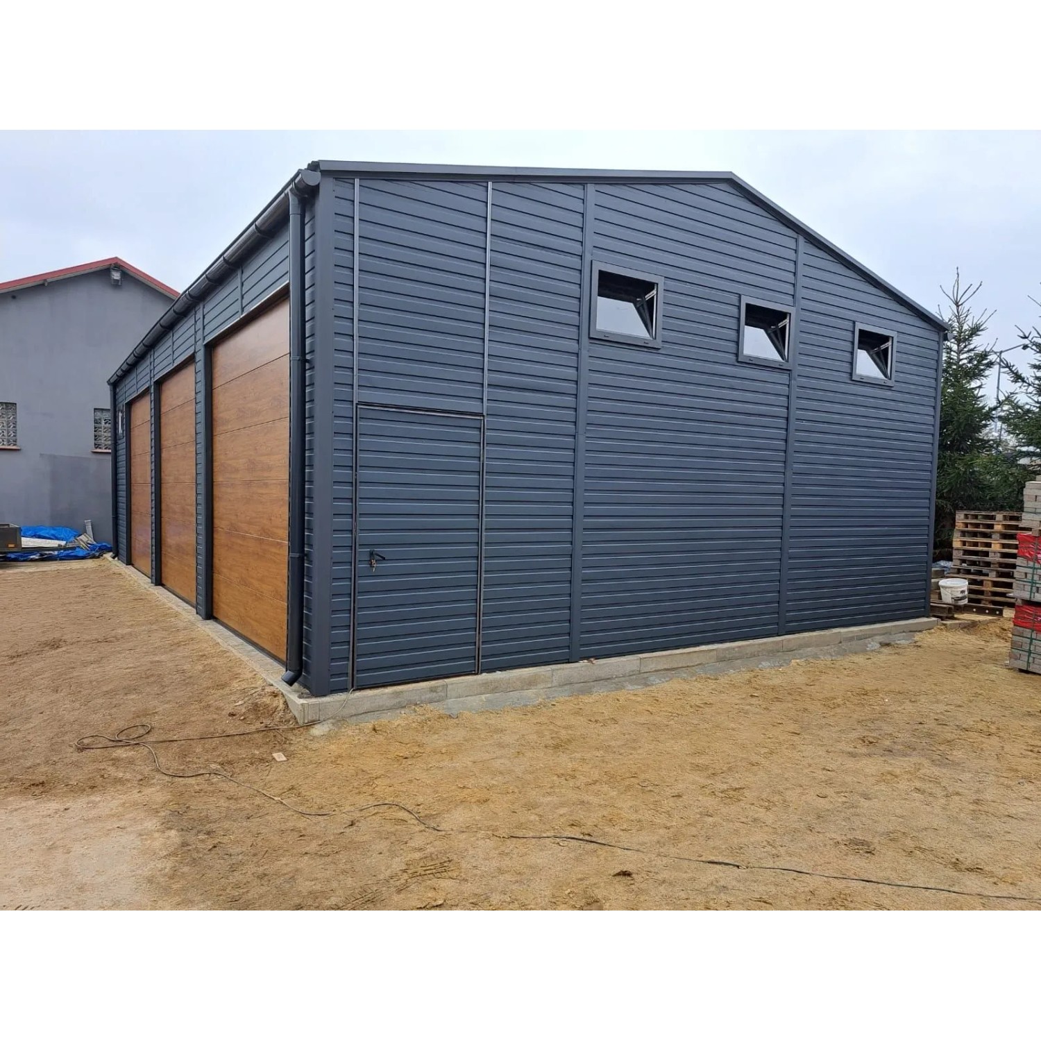 Liderstal Blechhalle 12x8m, graphit, mit drei Sektionaltoren in Goldene Eiche und kleinen Fenstern.