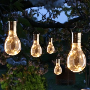 Fünf klare LED Solar Glühbirnen mit warmweißem Licht hängen im Garten an Ästen.