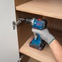 Hand mit Bosch Professional Akku-Bohrschrauber GSR18V-52 montiert Scharnier in Holzschrank. Kompaktes Akkugerät.