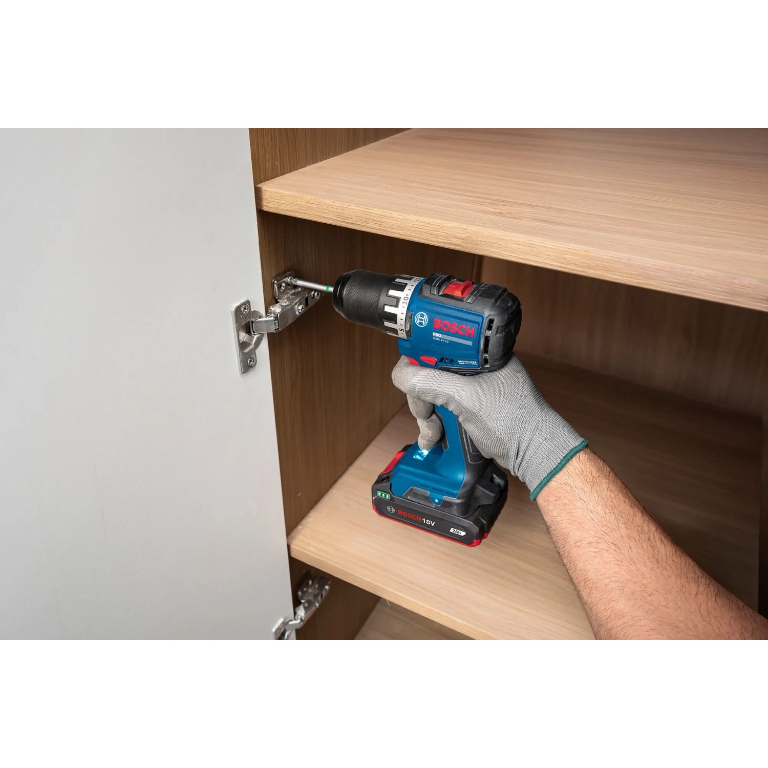 Hand mit Bosch Professional Akku-Bohrschrauber GSR18V-52 montiert Scharnier in Holzschrank. Kompaktes Akkugerät.