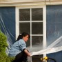 Frau deckt Fenster mit Tesa Easy Cover Universal Folie ab. Abdeckmaterialien für Renovierung.