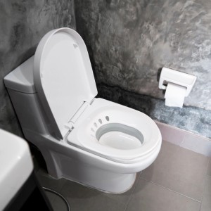 Zusammenklappbares, weißes Sitzbad aus Kunststoff auf einer Toilette im Badezimmer.