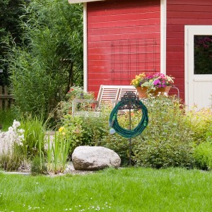 Freistehender, brauner Relaxdays Schlauchhalter aus Gusseisen im Garten mit Schlauch.
