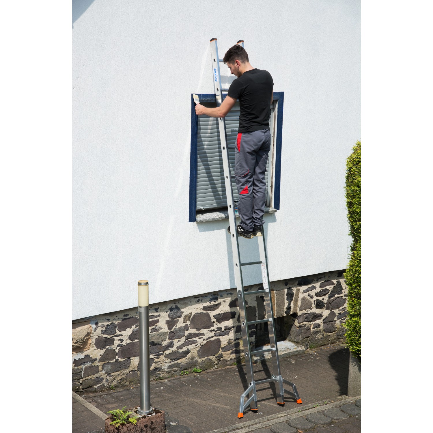 Krause Tribilo Vielzweckleiter 3x9 Sprossen im Einsatz vor einem Fenster an einer Hauswand.