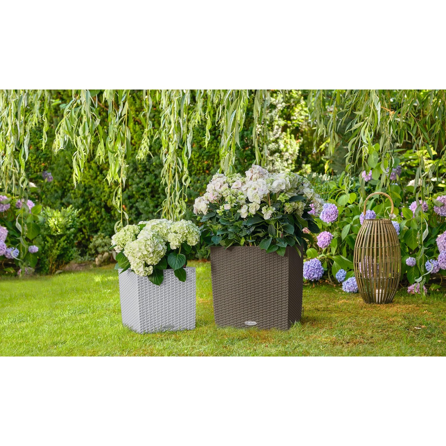 Lechuza Cube Cottage Pflanzgefäße, 30x30x30 cm, lichtgrau und braun, mit Pflanzen im Garten.