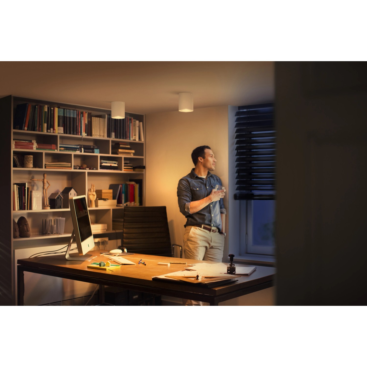 Szene mit Philips Hue Pillar LED-Aufbauspot in Weiß, der ein warmes Licht in einem Arbeitszimmer erzeugt.