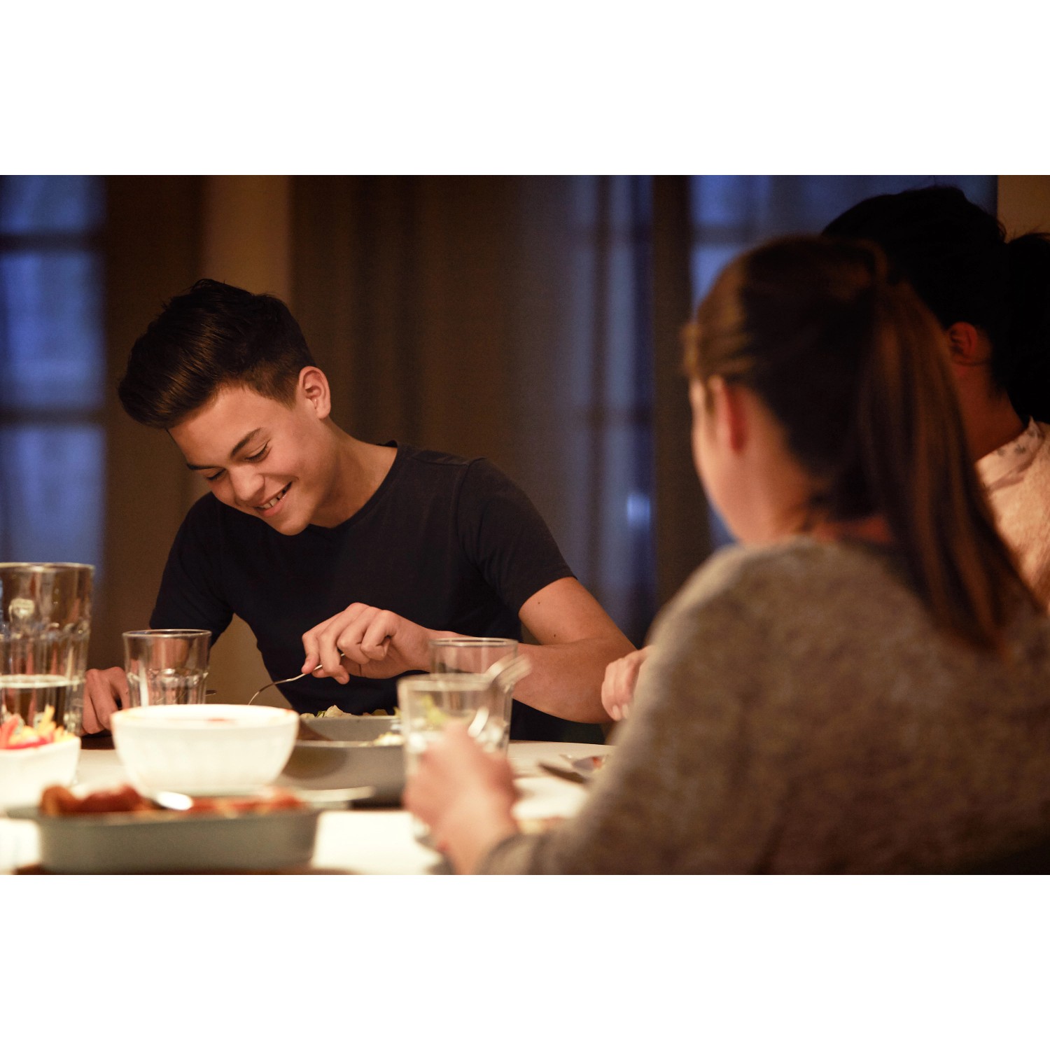 Szene mit warmem Licht durch Philips E14 LED Kerzen, Menschen beim Abendessen.