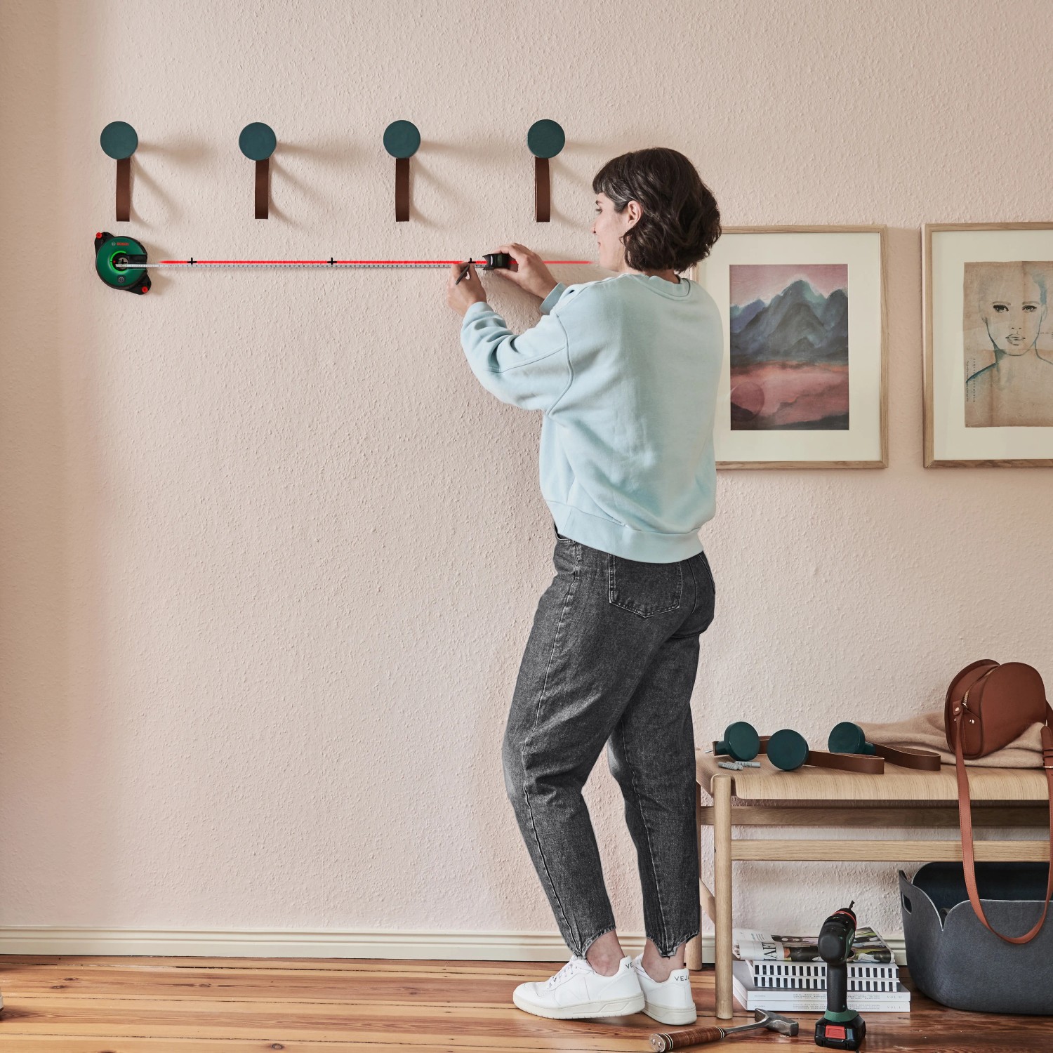 Frau misst mit Bosch Atino Linienlaser Wand für Anbringung von Haken aus.
