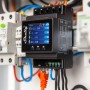 Schwarzes Shelly Relaismodul Pro 4PM zur Hausautomation mit Display und Kabelanschlüssen.