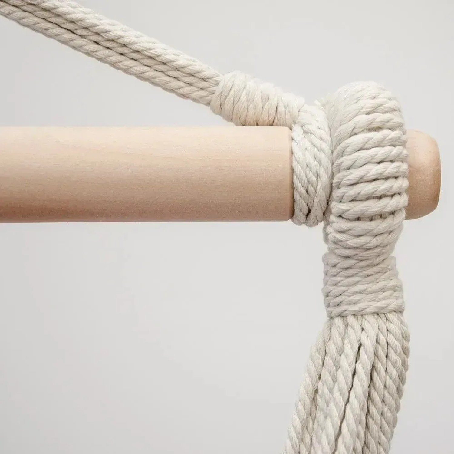 Detailansicht des hellen Holz-Spreizstabs eines AMANKA Hängesessels mit fest verknoteten, dicken Seilen.