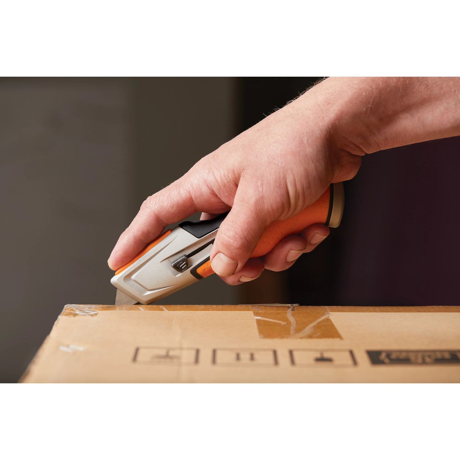 Hand schneidet Karton mit Fiskars Universalmesser CarbonMax™.