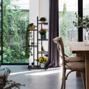 Schwarzes Stahl Blumenregal mit 6 Ablagen, bepflanzt, im modernen Wohnzimmer vor großem Fenster. Praktischer Pflanzenständer.