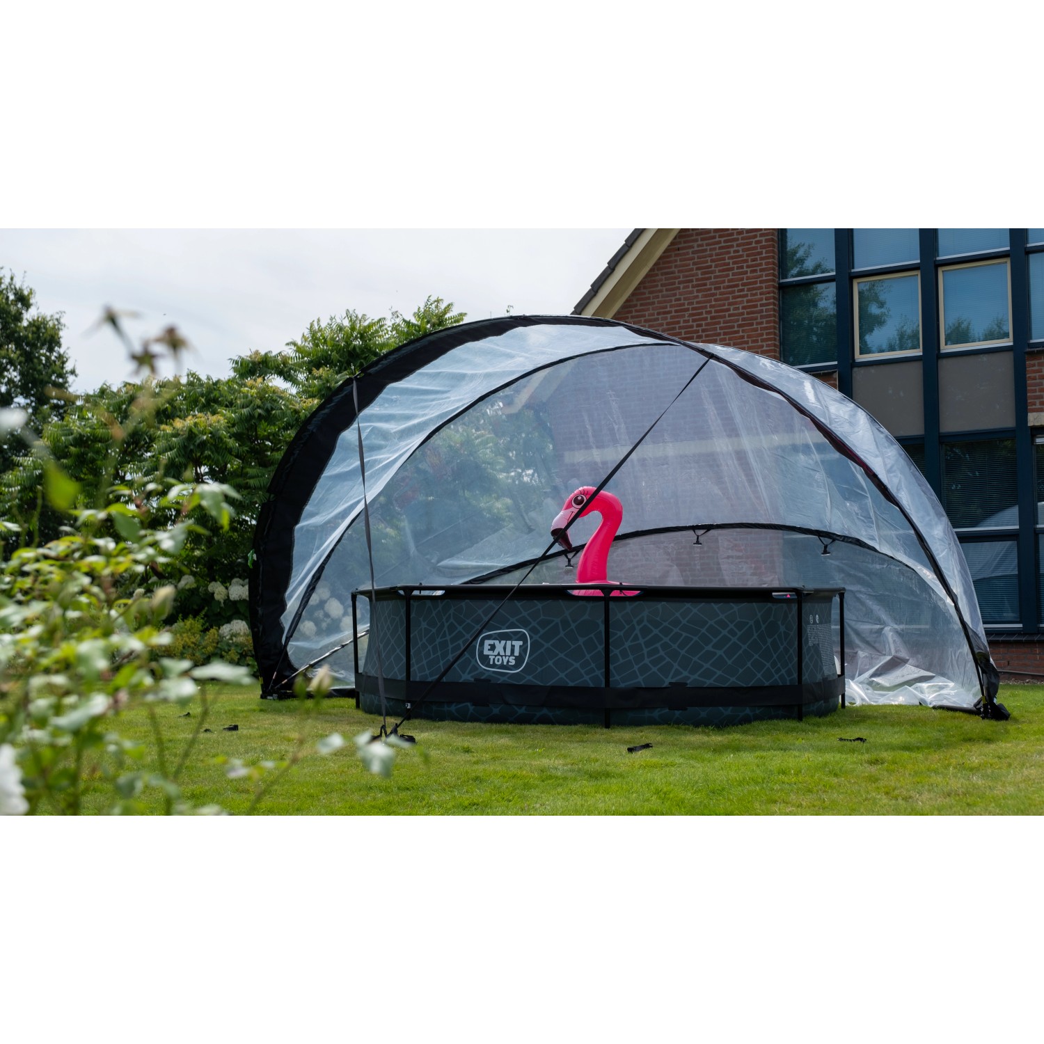 Exit Pool Abdeckung ECO Ø 550 cm auf Rasen mit Pool und pinkem Flamingo. Poolüberdachung schützt vor Wind und Wetter.
