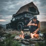 Petromax Dutch Oven Set am Lagerfeuer mit Outdoor-Abenteurer und Geländewagen mit Dachzelt.