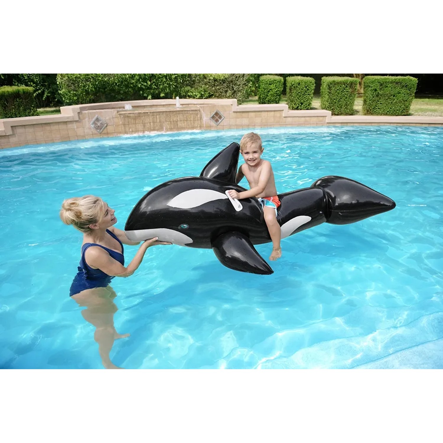 Kind auf Bestway Jumbo Wal Schwimmtier im Pool, begleitet von Erwachsenem. Aufblasbarer Wal in Schwarz-Weiß.