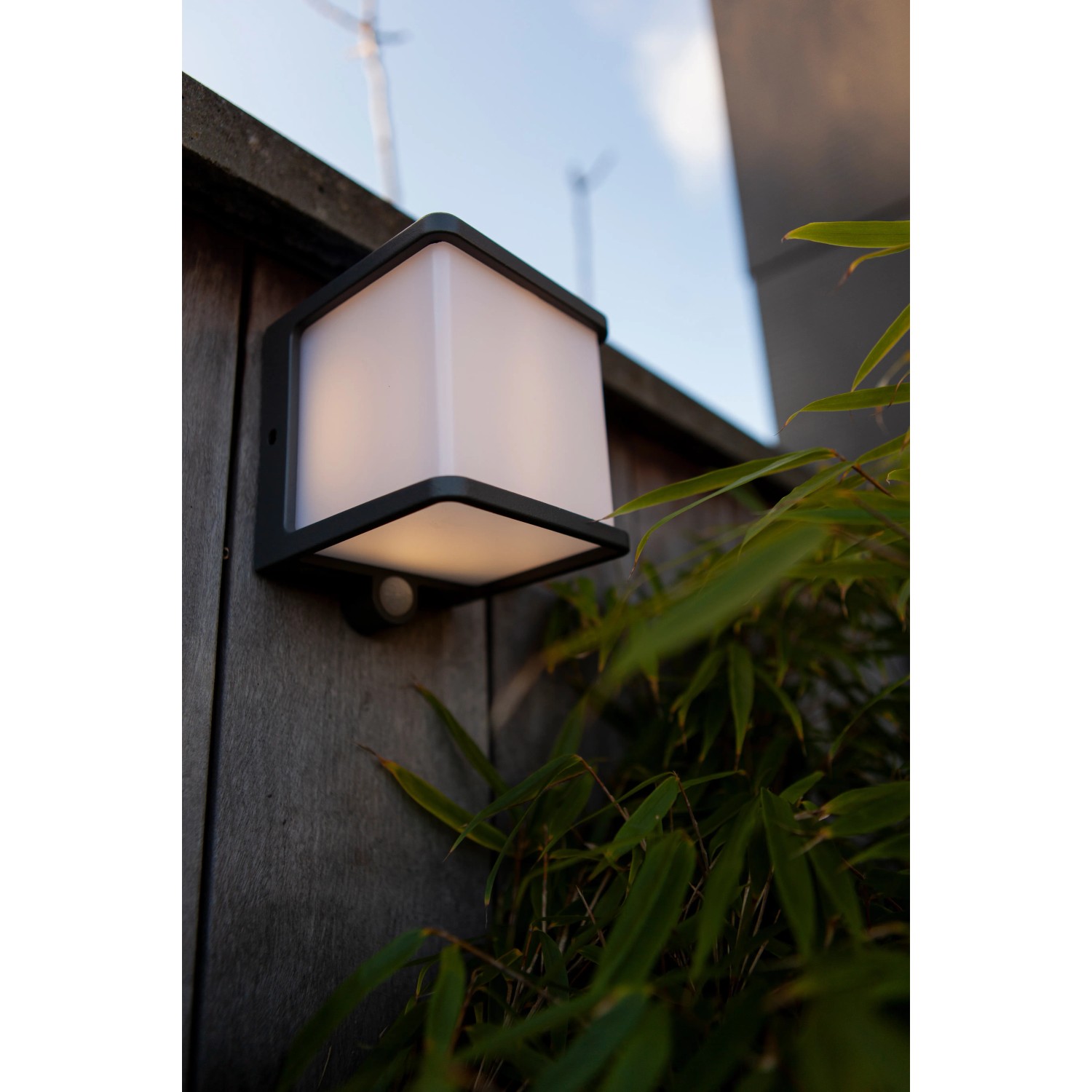 Anthrazitfarbene Lutec LED Solar Wandleuchte Doblo mit Bewegungsmelder an Holzwand.