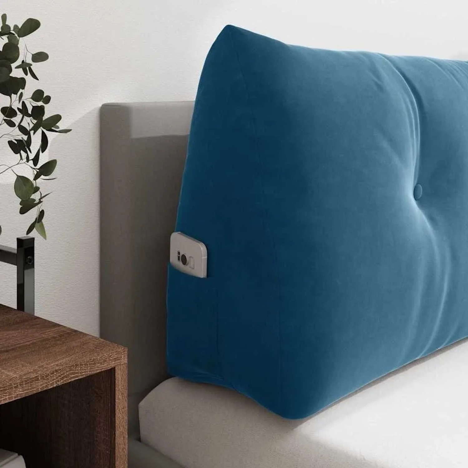 Blaues Samt-Rückenkissen mit Knöpfen und praktischer Seitentasche auf einem Bett. Ideal als bequeme Bettrückenlehne.