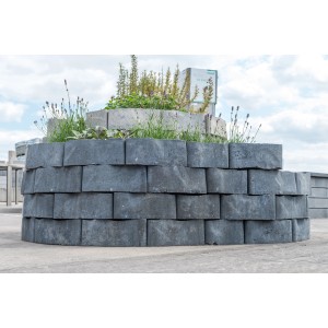 Runde Mauer aus grauen Diephaus Epocca Quarzit Mauertrapezsteinen mit Bepflanzung.