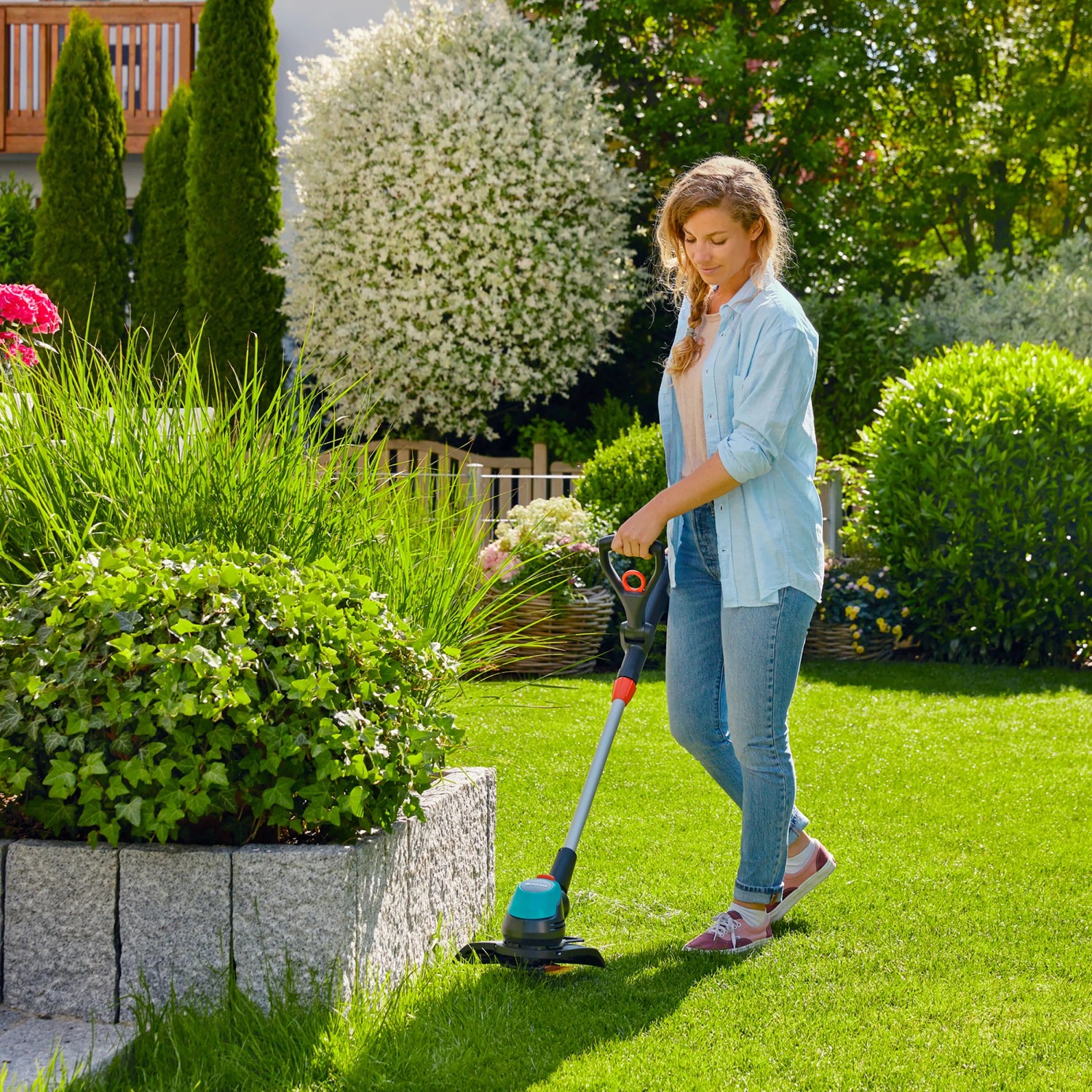 Frau trimmt Rasen mit Gardena Akku-Trimmer EasyCut 23/18V P4A im Garten.