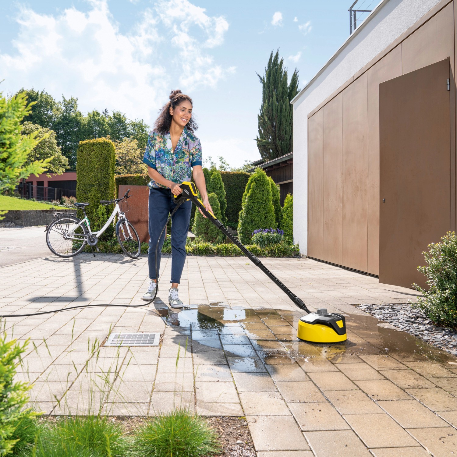 Frau reinigt Pflaster mit gelbem Kärcher Flächenreiniger T 5 T-Racer und Hochdruckreiniger.
