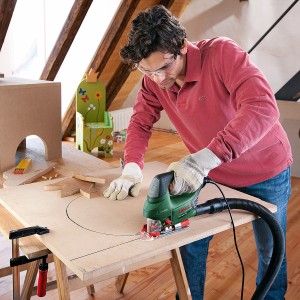 Mann sägt Kreis mit Bosch Stichsäge PST 900 PEL in Holzplatte. Staubabsaugung angeschlossen.