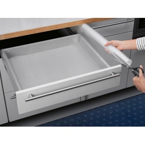 Transparente Schubladenmatte wird mit einer Schere zugeschnitten in einer Küchenschublade.