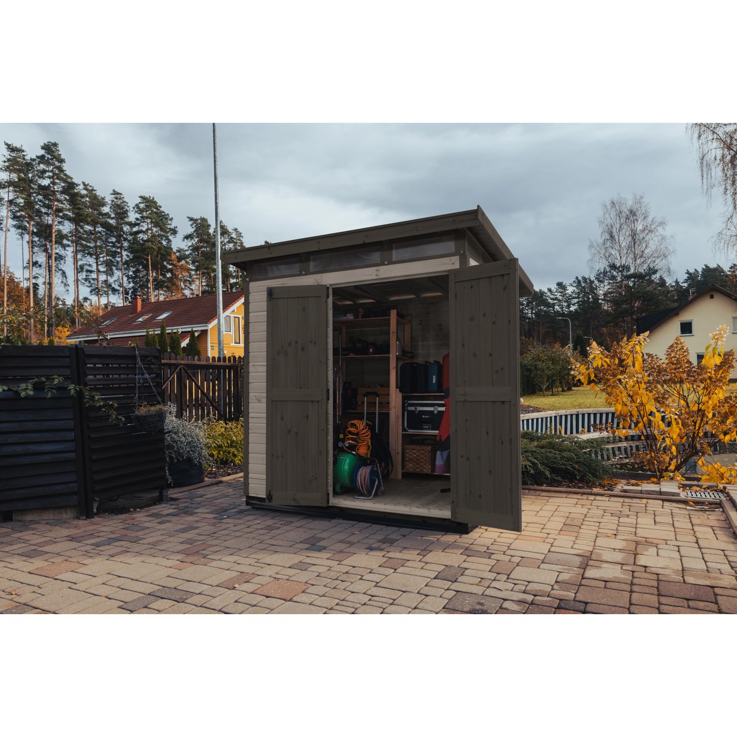 Graues Upyard Gartenhaus Strongbox L mit geöffneten Doppeltüren und Fundament im Garten.