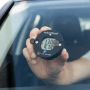 Hand hält schwarze Technaxx TX-353 Mini-Parkscheibe mit digitaler Zeitanzeige 12:00 an Autoscheibe. Automatische Parkzeit.