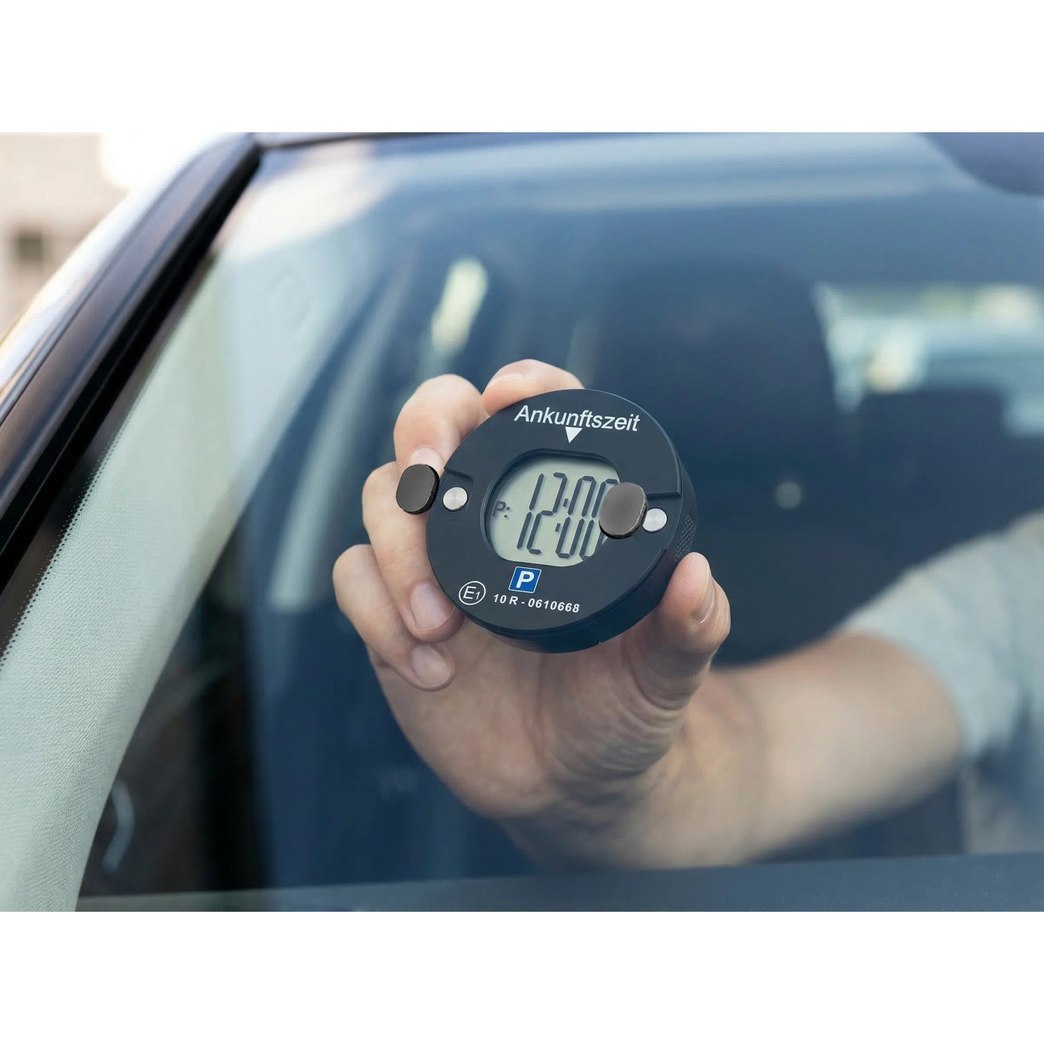 Hand hält schwarze Technaxx TX-353 Mini-Parkscheibe mit digitaler Zeitanzeige 12:00 an Autoscheibe. Automatische Parkzeit.