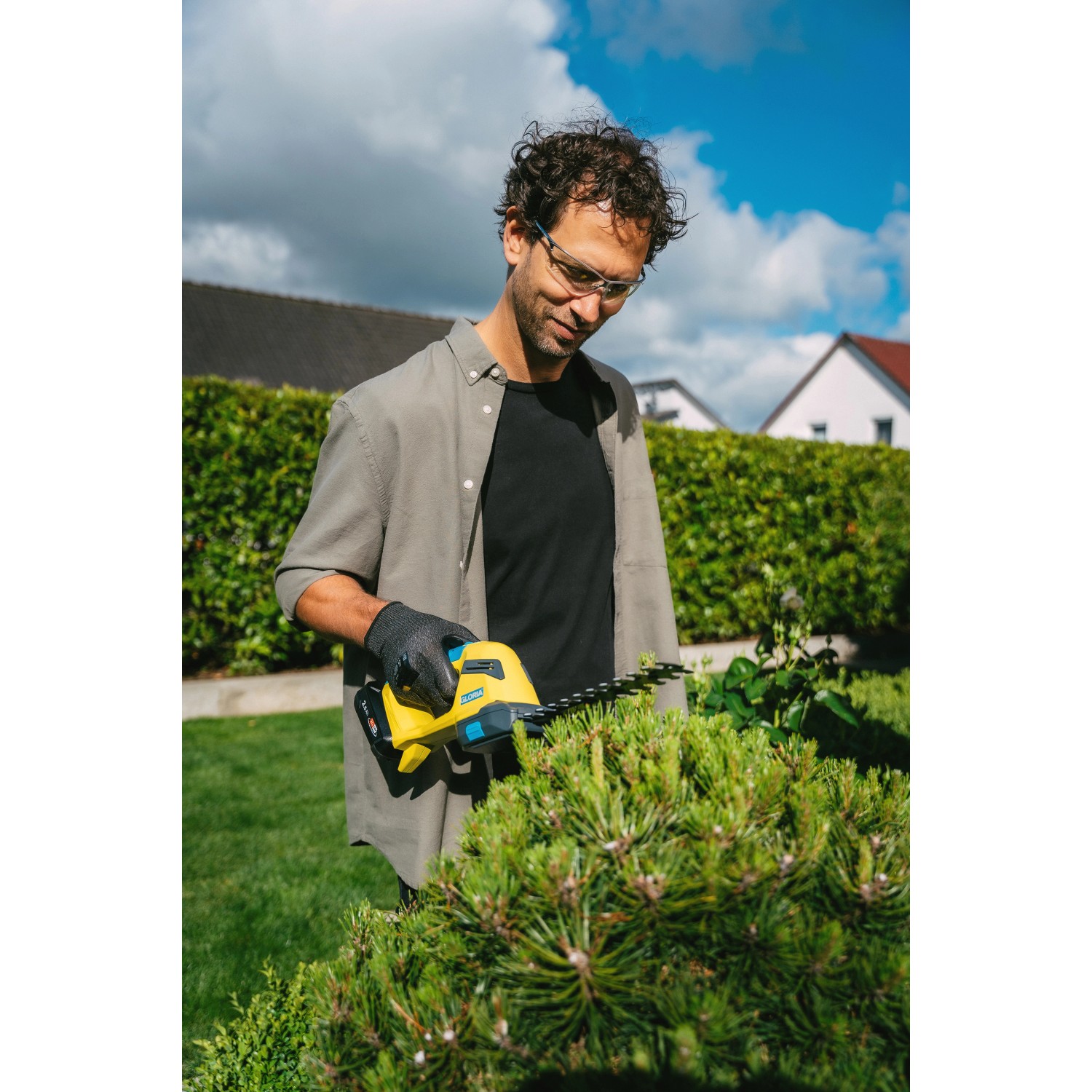 Mann schneidet Strauch mit gelber Gloria Akku-Gras- und Strauchschere FineCut Compact.