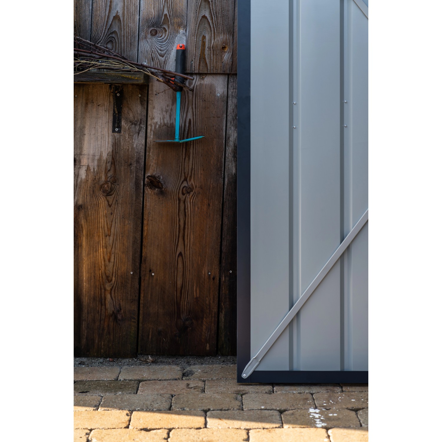 Detailansicht: Anthrazitfarbenes Globel Metall-Anlehngerätehaus Lean-To mit Gartengerät an Holzwand.