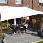 Cremeweißes Floracord Vierecksonnensegel aus HDPE über einer Terrasse mit Tisch und Stühlen.