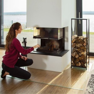 Hohes, schwarzes Stahl Kaminholzregal neben modernem Kamin, gefüllt mit Holzscheiten. Ideal für Kaminzubehör.