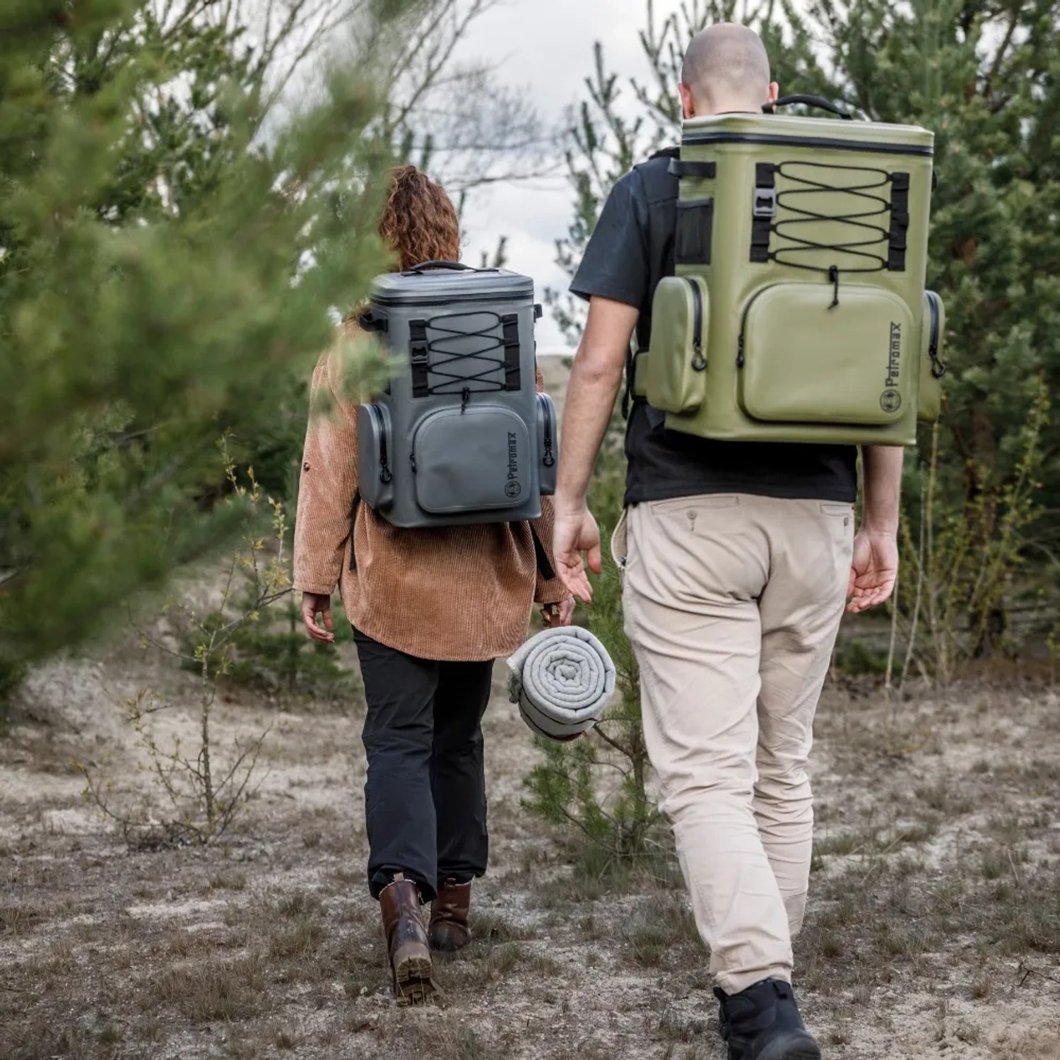 Zwei Personen mit Petromax Kühlrucksäcken (grau/oliv) beim Wandern in der Natur.