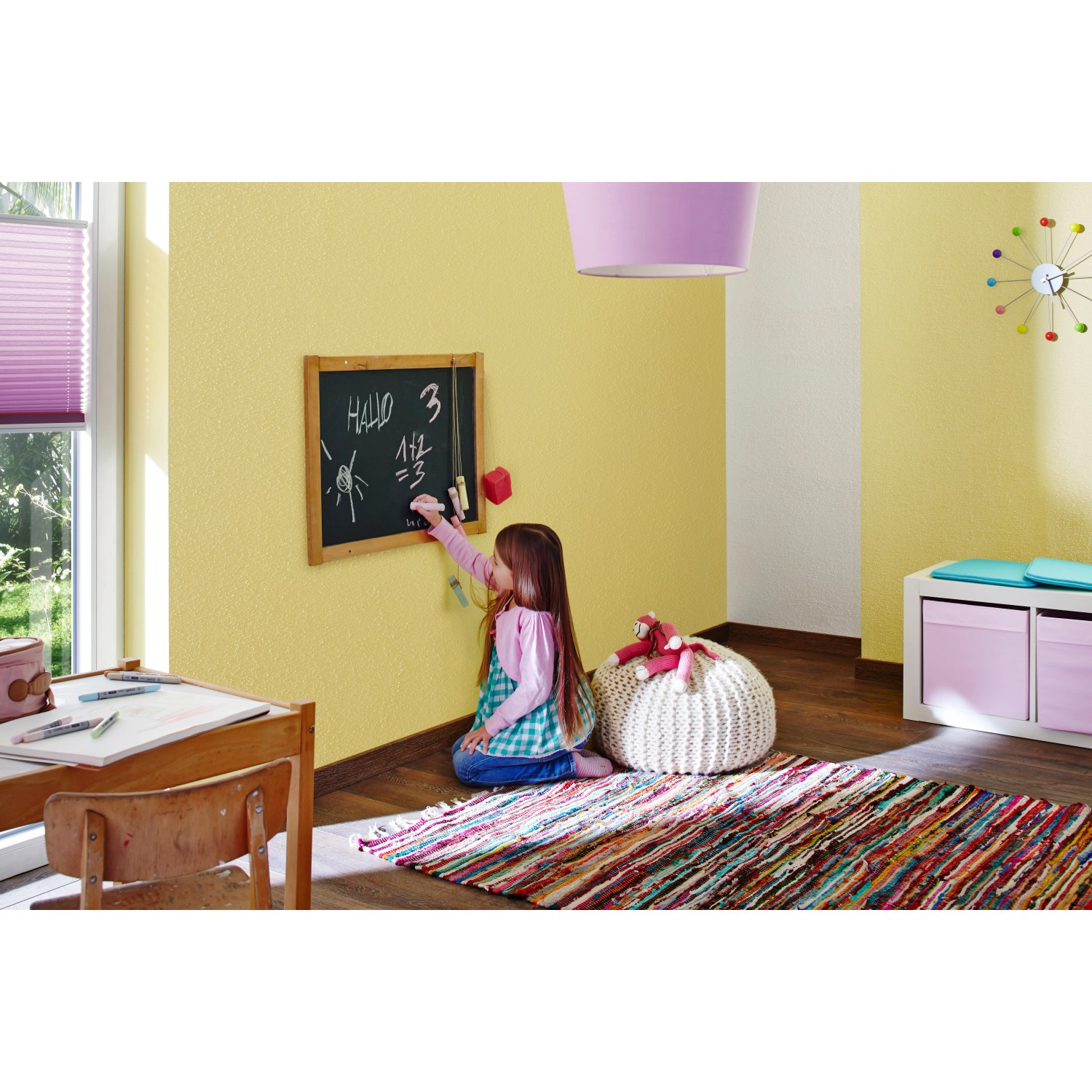 Kinderzimmer mit Wand in Zitronengelb, gestaltet mit Knauf Compact Color. Mädchen malt auf Tafel.