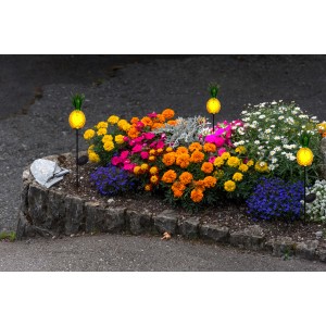 Orangefarbener LED-Solar-Erdspieß Ananas (81 cm) als Deko im Blumenbeet.