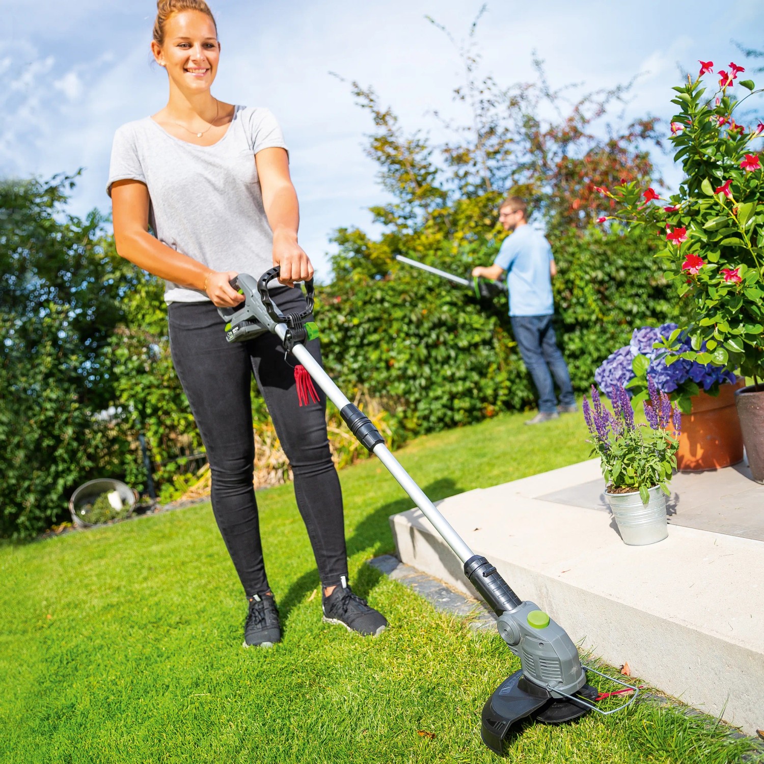 Frau trimmt Rasen mit LUX Akku-Rasentrimmer A-RT-20/26 1 PowerSystem im Garten.