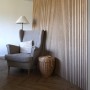 Denpanels Akustikpaneel Eiche Beige: Raum mit Sessel und Korb vor der Holzpaneel-Wand.