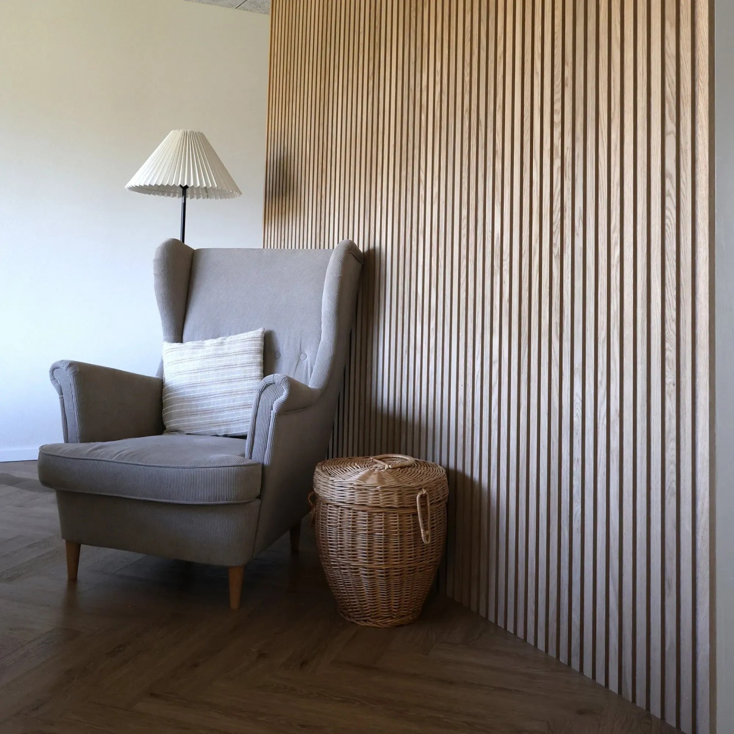 Denpanels Akustikpaneel Eiche Beige: Raum mit Sessel und Korb vor der Holzpaneel-Wand.
