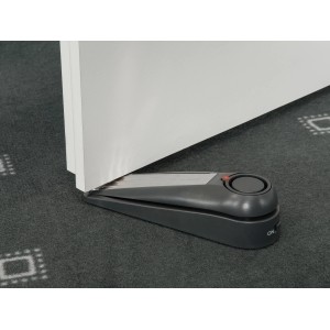 Grauer Türstopper-Alarm unter einer Tür auf einem Teppich. Alarmanlage für mehr Sicherheit.