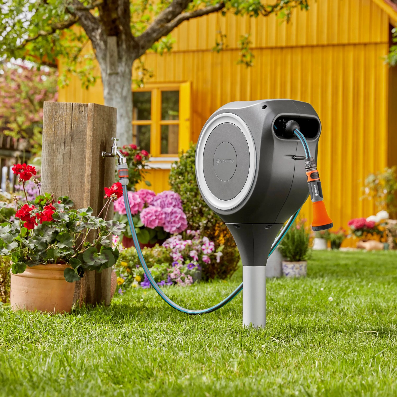 Gardena RollUp M Gartenschlauchbox mit 20m Schlauch im Garten, mit Wasserhahn verbunden.