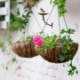 Braune Gusseisen Vogeltränke mit dekorativer Vogelfigur, an weißer Wand über Blumenampeln im Garten oder auf dem Balkon.